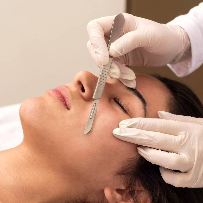 Therapist dermaplaning a client's cheek with a fine surgical blade
