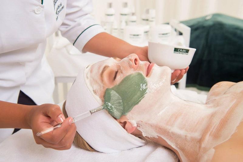 Therapist brushing a green DMK enzyme mask onto a client's face