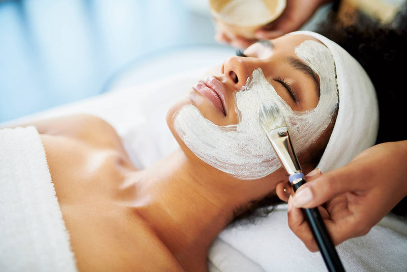 Therapist applying a face mask with a brush during a facial